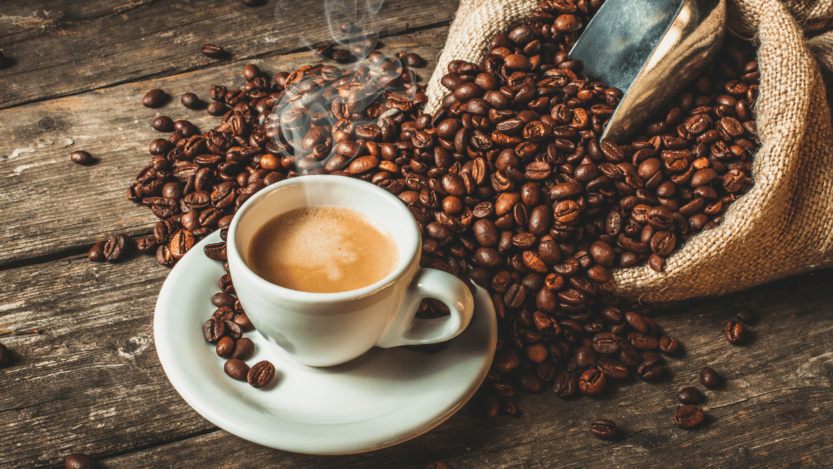 A steaming cup of coffee surrounded by coffee beans