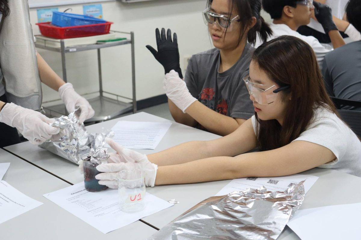 Claire Shin (9) and Abigale Kim (9) perform a redox reaction with copper chloride and aluminum foil for the Science Club trial meet.